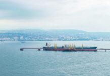 Oil tanker docked at a shipping port with a coastal city in the background