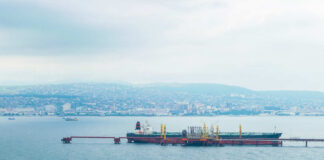 Oil tanker docked at a shipping port with a coastal city in the background