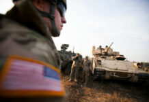 Soldiers in military gear coordinating near armored vehicles during training