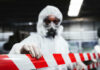 Worker in protective gear holding a red and white barrier tape in an industrial environment
