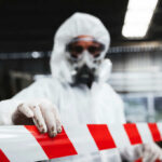 Hidden Tank Sparks Massive Evacuations Worker in protective gear holding a red and white barrier tape in an industrial environment