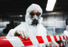 Hidden Tank Sparks Massive Evacuations Worker in protective gear holding a red and white barrier tape in an industrial environment