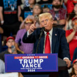 Donald Trump speaking at a political rally with a crowd in the background