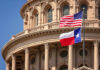 American and Texas flags flying in front of a state capitol building