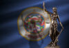 Bronze statue of Lady Justice holding scales in front of the Minnesota state flag