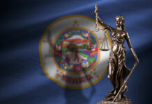 Bronze statue of Lady Justice holding scales in front of the Minnesota state flag