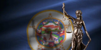 Bronze statue of Lady Justice holding scales in front of the Minnesota state flag