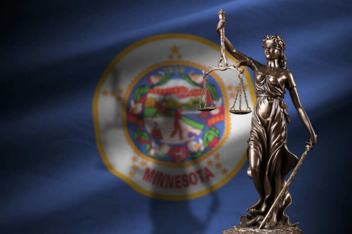 Bronze statue of Lady Justice holding scales in front of the Minnesota state flag