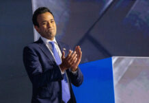 A man in a suit clapping on stage during a presentation