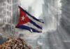 Is US’s Plan Pushing Cuba to Collapse? Tattered Cuban flag waving over a pile of rubble in a devastated urban landscape