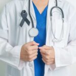 Healthcare professional wearing a white coat and stethoscope, with a black ribbon on their chest