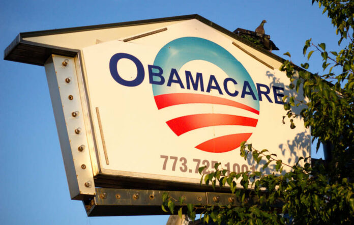 Sign displaying Obamacare with a blue and red logo against a clear sky