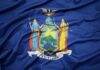 Tax-The-Rich Wave Rocks Democrats New York State flag with coat of arms on blue field