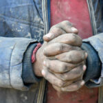 Close-up of dirty hands clasped together, wearing a blue jacket
