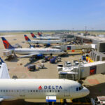View of multiple Delta Airlines planes parked at an airport terminal with ground crew and vehicles