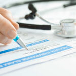 Staggering $9B Question: AG Bolts A hand holding a pen writing on a health insurance claim form with a stethoscope in the background
