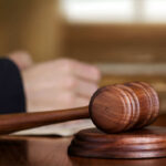 Murder Convict Wants Taxpayer-Funded Appeal A wooden gavel on a desk with a blurred hand in the background reviewing documents