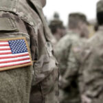 Close-up of a soldiers uniform with an American flag patch, surrounded by other soldiers