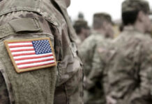 Close-up of a soldiers uniform with an American flag patch, surrounded by other soldiers
