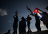 Cuba Opens Markets Amid Deep Crisis Silhouetted figures celebrating with a trophy and Cuban flags against a sunset sky
