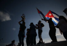 Cuba Opens Markets Amid Deep Crisis Silhouetted figures celebrating with a trophy and Cuban flags against a sunset sky