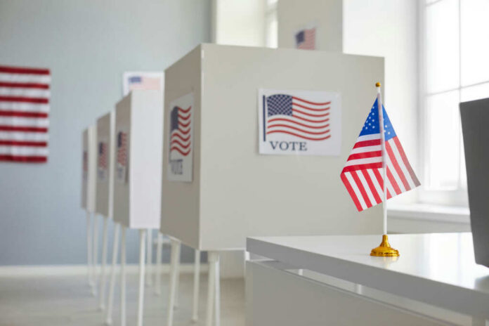 shutterstock_2407412213 Voting booths with American flags in a polling station