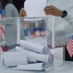 Person casting a vote into a transparent ballot box during an election