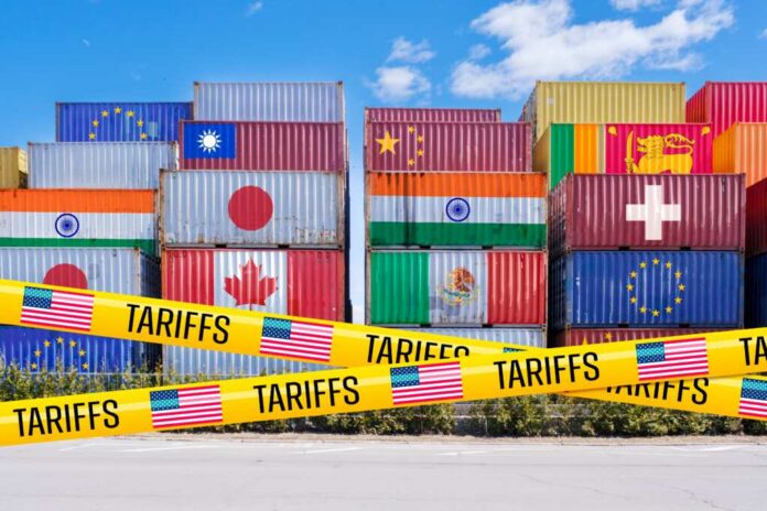 Stacked shipping containers with national flags behind yellow tariffs tape