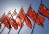 Multiple Chinese flags waving against a clear blue sky with sunlight in the background