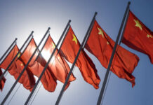 Airport Stop Turns Into Spy Nightmare Multiple Chinese flags waving against a clear blue sky with sunlight in the background