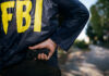 Most Wanted List Delivers First Bust FBI agent gripping handgun near waistband outdoors