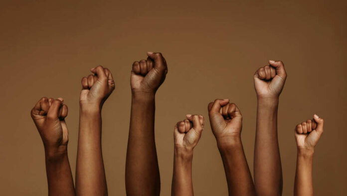 shutterstock1830702032jpg-1 A group of diverse hands with raised fists against a brown background