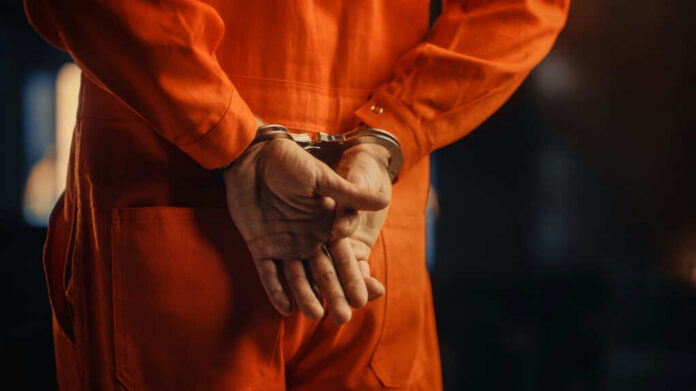 shutterstock2056434935jpg Individual in an orange jumpsuit with hands cuffed behind their back