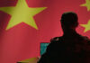 Declassified Files Reveal China Activity Silhouette of a military personnel working on a laptop in front of a Chinese flag