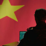 Silhouette of a military personnel working on a laptop in front of a Chinese flag