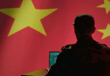 Declassified Files Reveal China Activity Silhouette of a military personnel working on a laptop in front of a Chinese flag