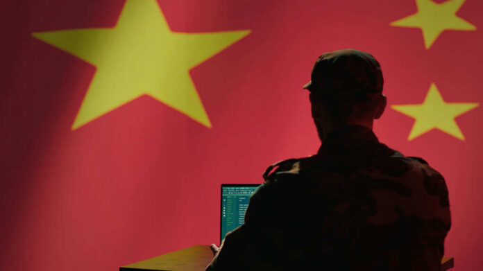 shutterstock2500332477jpg Silhouette of a military personnel working on a laptop in front of a Chinese flag