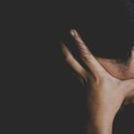 NYU Firestorm Over ‘Suicidal Empathy’ person covering face with hand in dark background