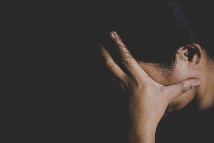 shutterstock_1023504136 person covering face with hand in dark background