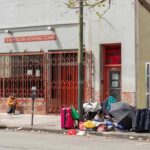 Sidewalk scene outside a housing clinic with people and belongings