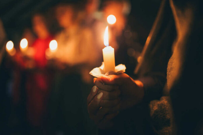 shutterstock_1174053094 People holding lit candles in a dimly lit setting
