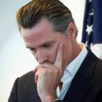 Is Newsom Right About Capitalism’s Failures? man in suit touching his face thoughtfully