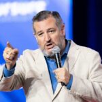 A man in a light suit passionately speaking into a microphone at a conference