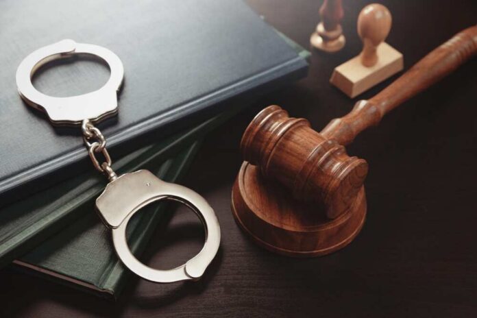 Arrest,Concept.,Metal,Handcuffs,Near,Judge,Gavel.,Law,And,Justice Handcuffs and a gavel on a desk with legal books