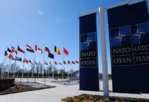 NATO Demands 5% Spending Plans Flags of various nations displayed outside NATO headquarters under a clear blue sky