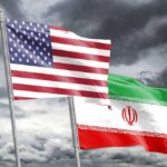 Flags of the United States and Iran waving against a cloudy sky