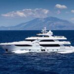 Luxury motor yacht cruising on blue sea with mountains in background