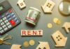 Rent payment concept with calculator, cash roll, coins, keys, and wooden house icons