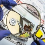 Forensic technician examining an open hard drive with a magnifying glass