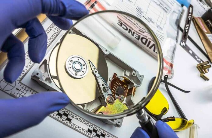 shutterstock_1375388630 Forensic technician examining an open hard drive with a magnifying glass